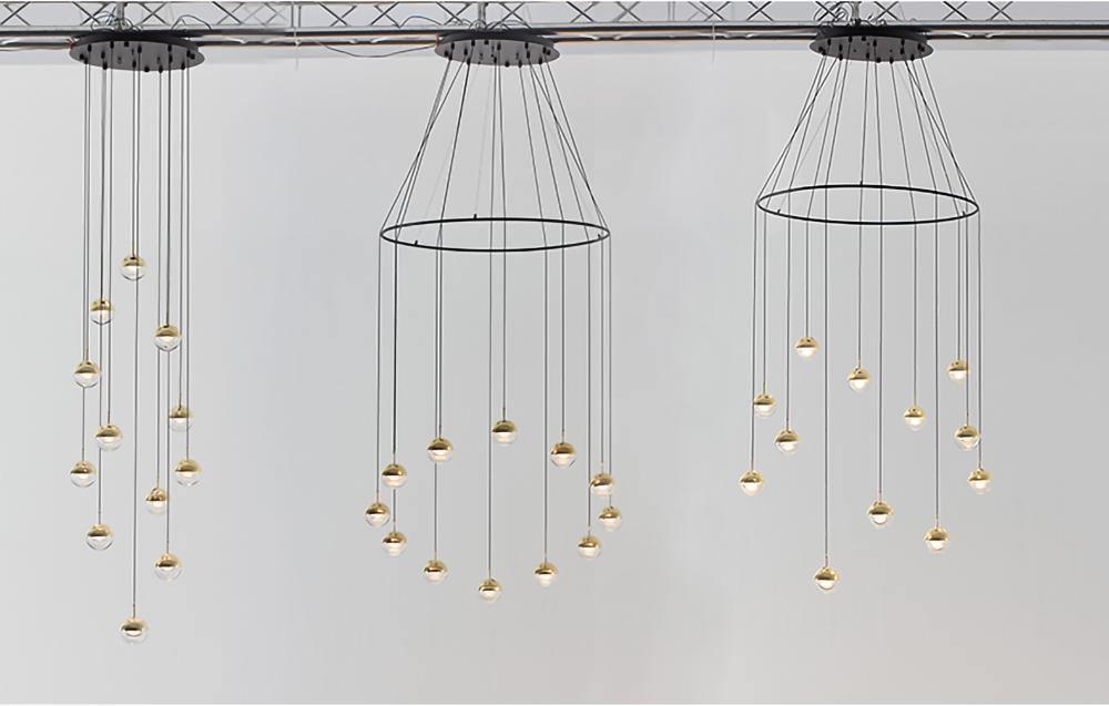 Three Clérachic ring chandeliers with small gold-finish globe pendants, seen against a white wall under a ceiling truss.