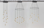 Three Clérachic ring chandeliers with small gold-finish globe pendants, seen against a white wall under a ceiling truss.