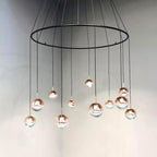 Clérachic ring chandelier with rose gold and clear globe pendants hung at varied heights from thin black cords.