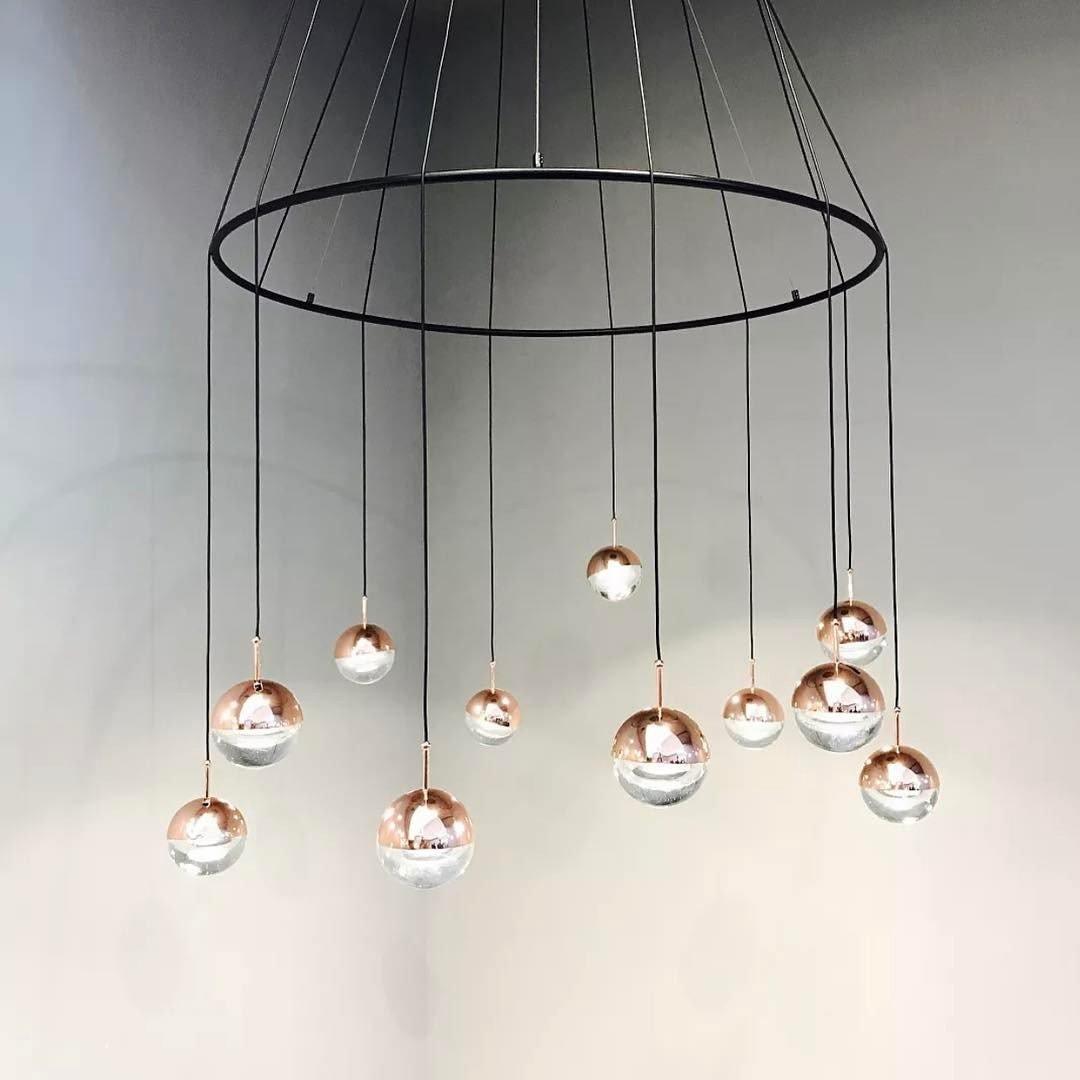 Clérachic ring chandelier with rose gold and clear globe pendants hung at varied heights from thin black cords.