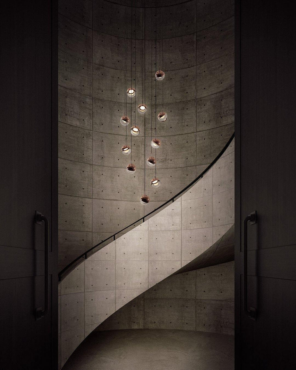 Rose gold Clérachic globe pendants hung at stepped heights down a spiral concrete stairwell, lit from within.
