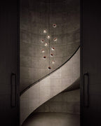 Rose gold Clérachic globe pendants hung at stepped heights down a spiral concrete stairwell, lit from within.