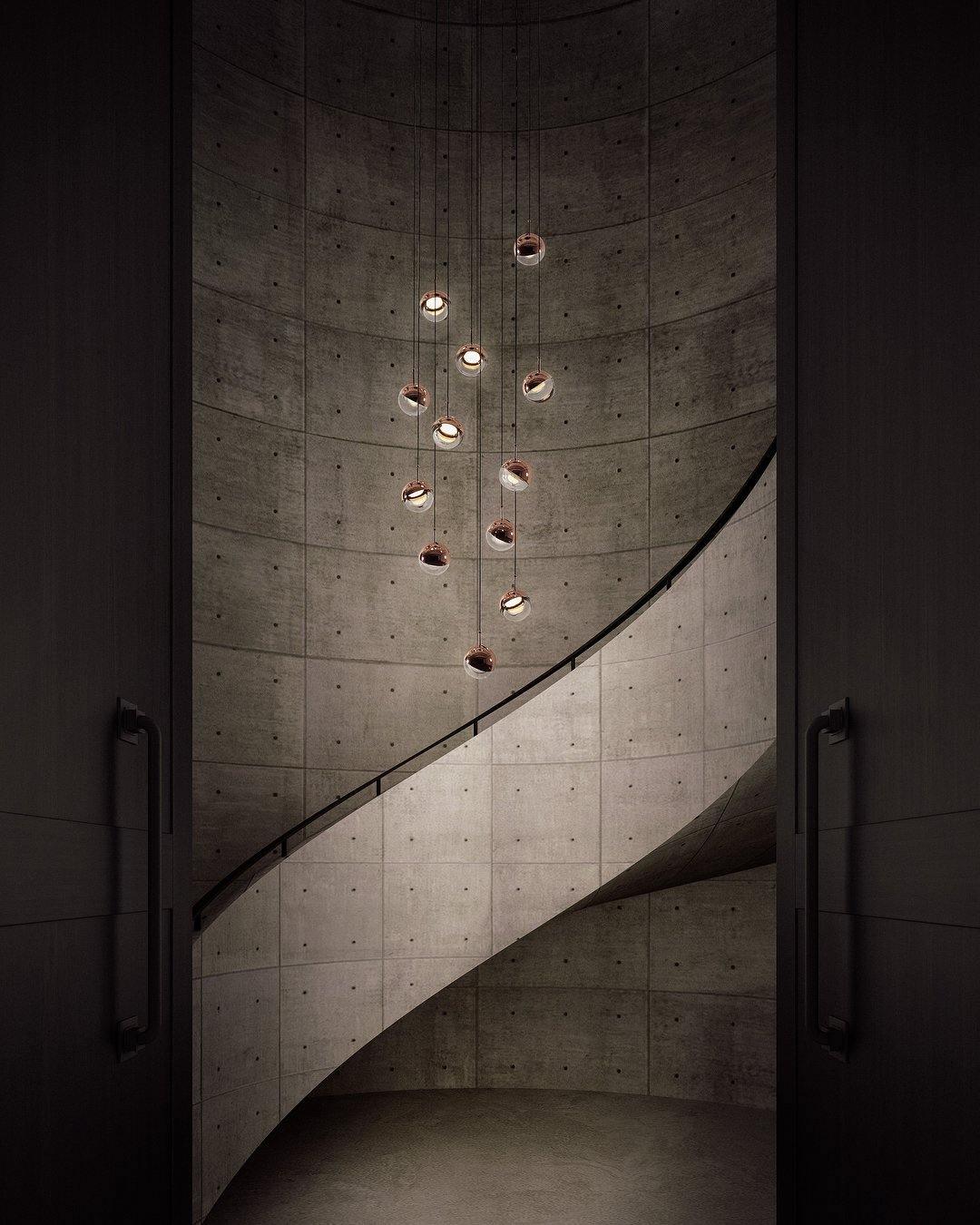 Rose gold Clérachic globe pendants hung at stepped heights down a spiral concrete stairwell, lit from within.