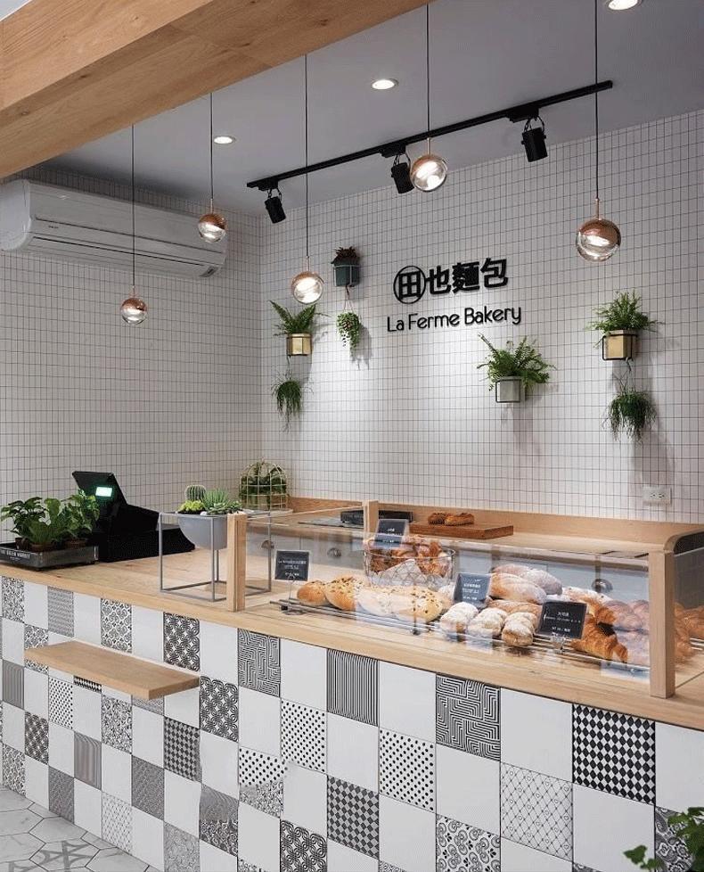 Rose gold Clérachic globe pendants hung over a bakery counter with white tiles, plants and track lighting.