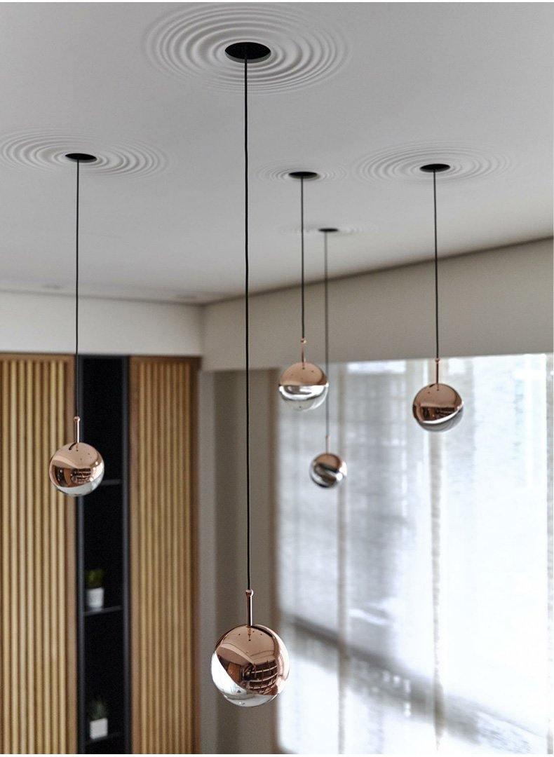 Rose gold Clérachic globe pendants at different heights in a room with slatted wood panelling and a large window.