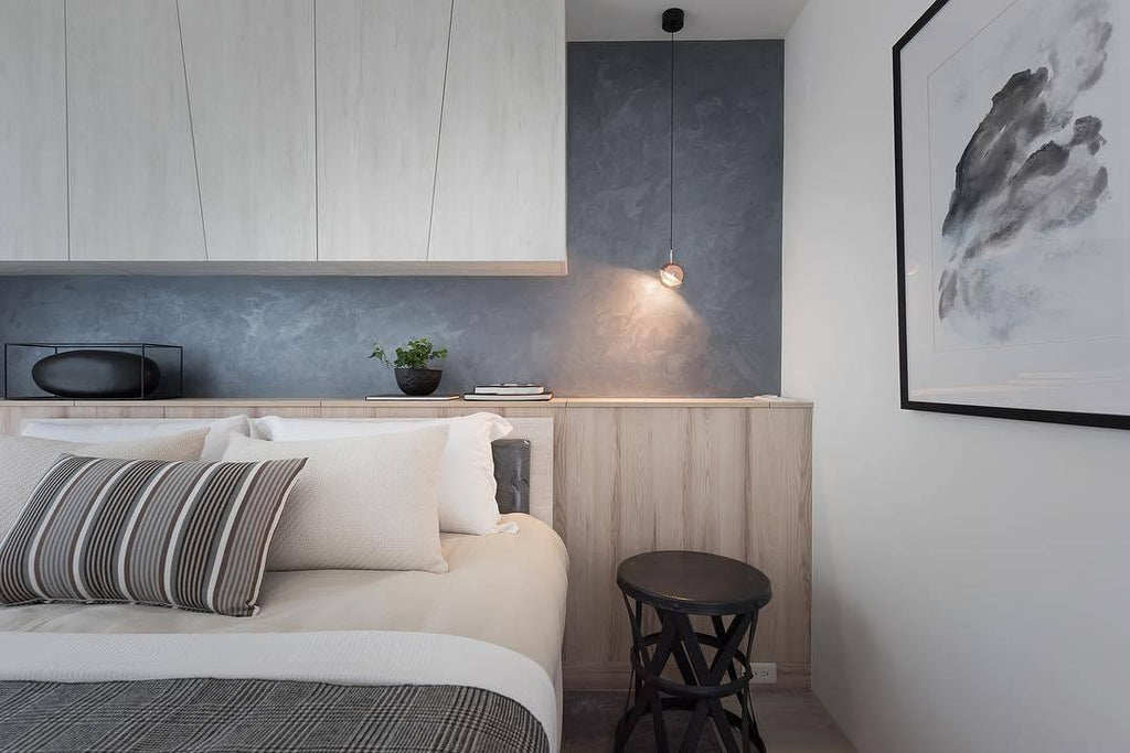 Single gold-finish Clérachic globe pendant on a short drop beside a bed, with a grey feature wall and a framed print.