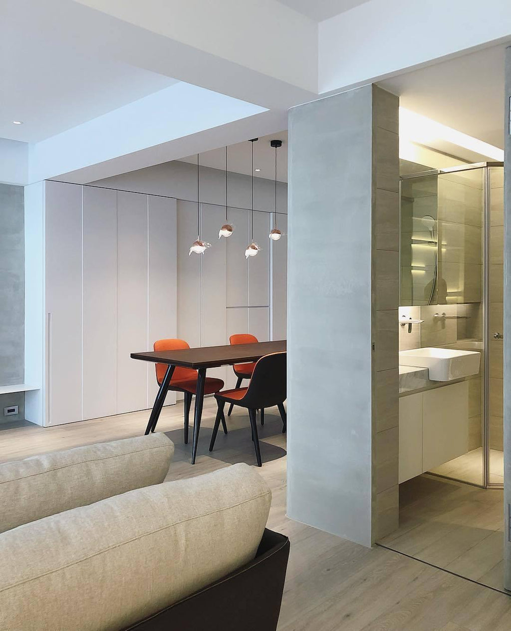 Clérachic globe pendants hung in a group above a dark dining table with orange chairs, beside a bathroom doorway.