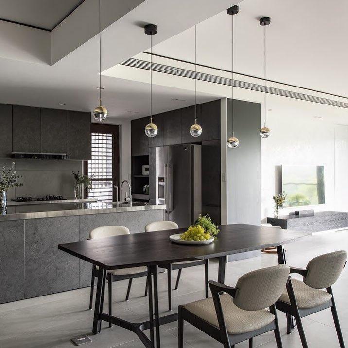 Four gold-finish Clérachic globe pendants over a dark dining table with grey chairs and a dark kitchen island.