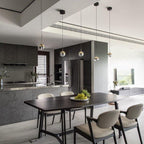 Four gold-finish Clérachic globe pendants over a dark dining table with grey chairs and a dark kitchen island.