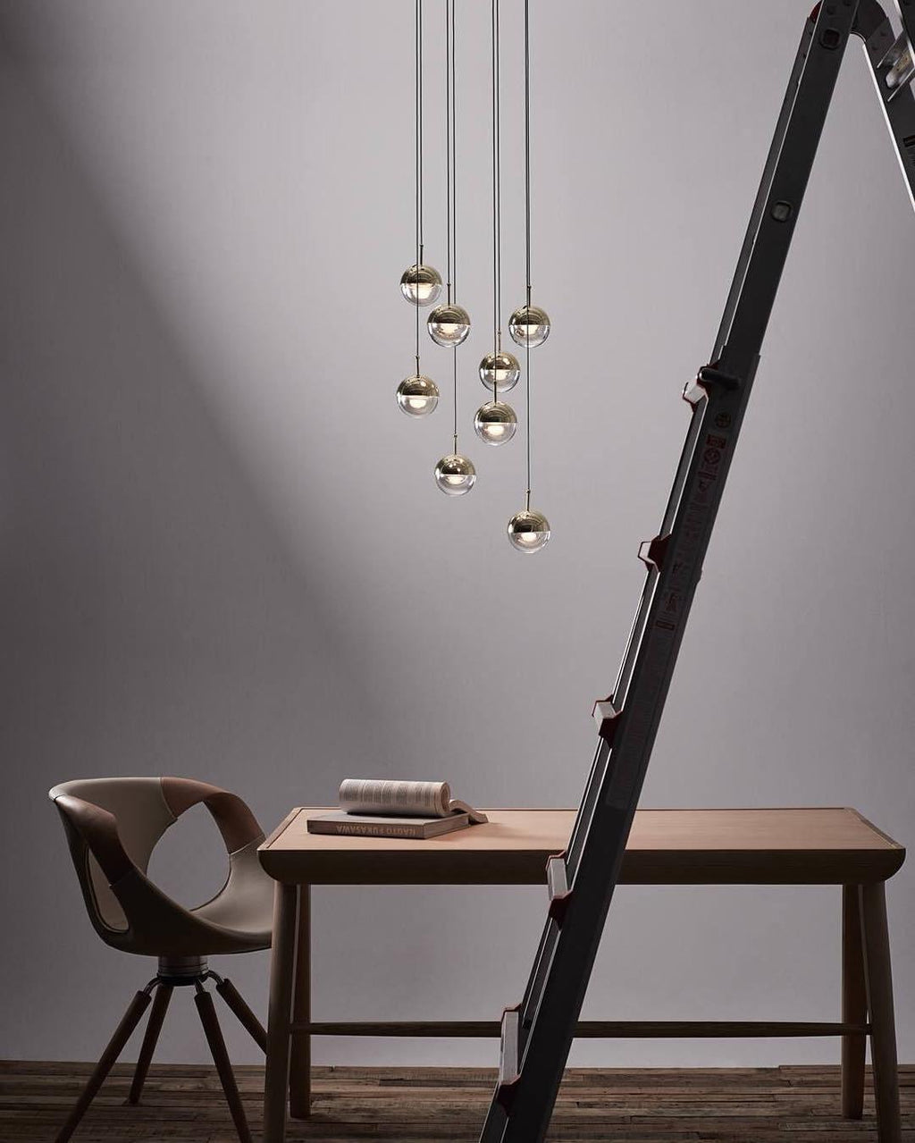 Cluster of Clérachic globe pendants in a stepped group on a grey wall, above a wooden desk, a chair and a ladder.