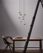 Cluster of Clérachic globe pendants in a stepped group on a grey wall, above a wooden desk, a chair and a ladder.