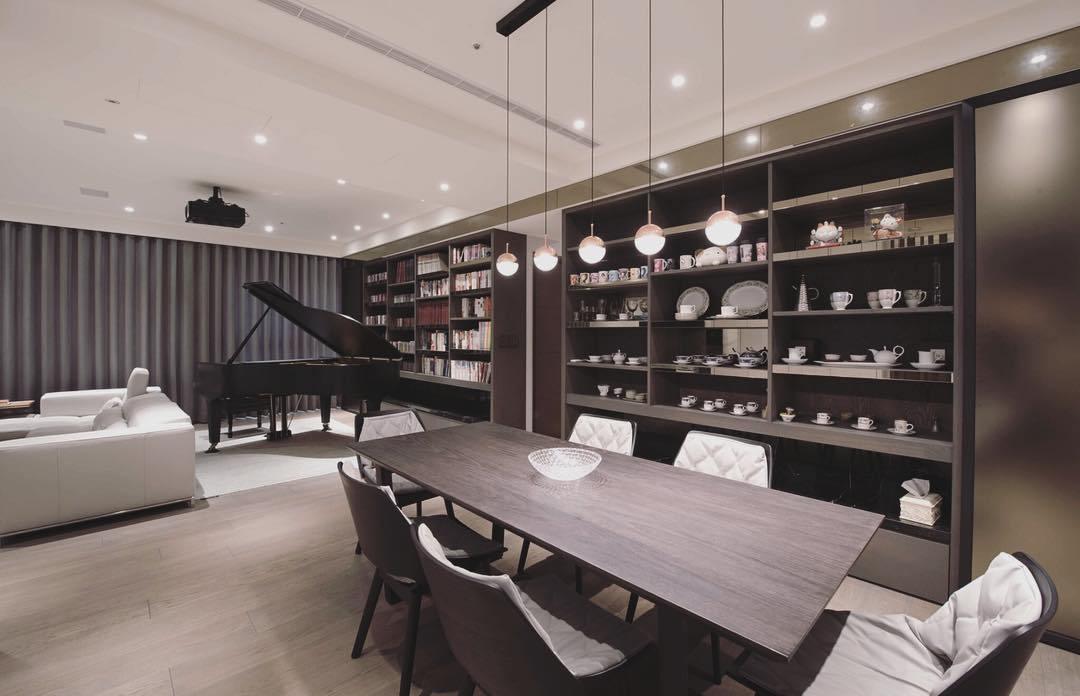 Small Clérachic pendants hung over a long dark dining table in a room with a grand piano and display shelves.