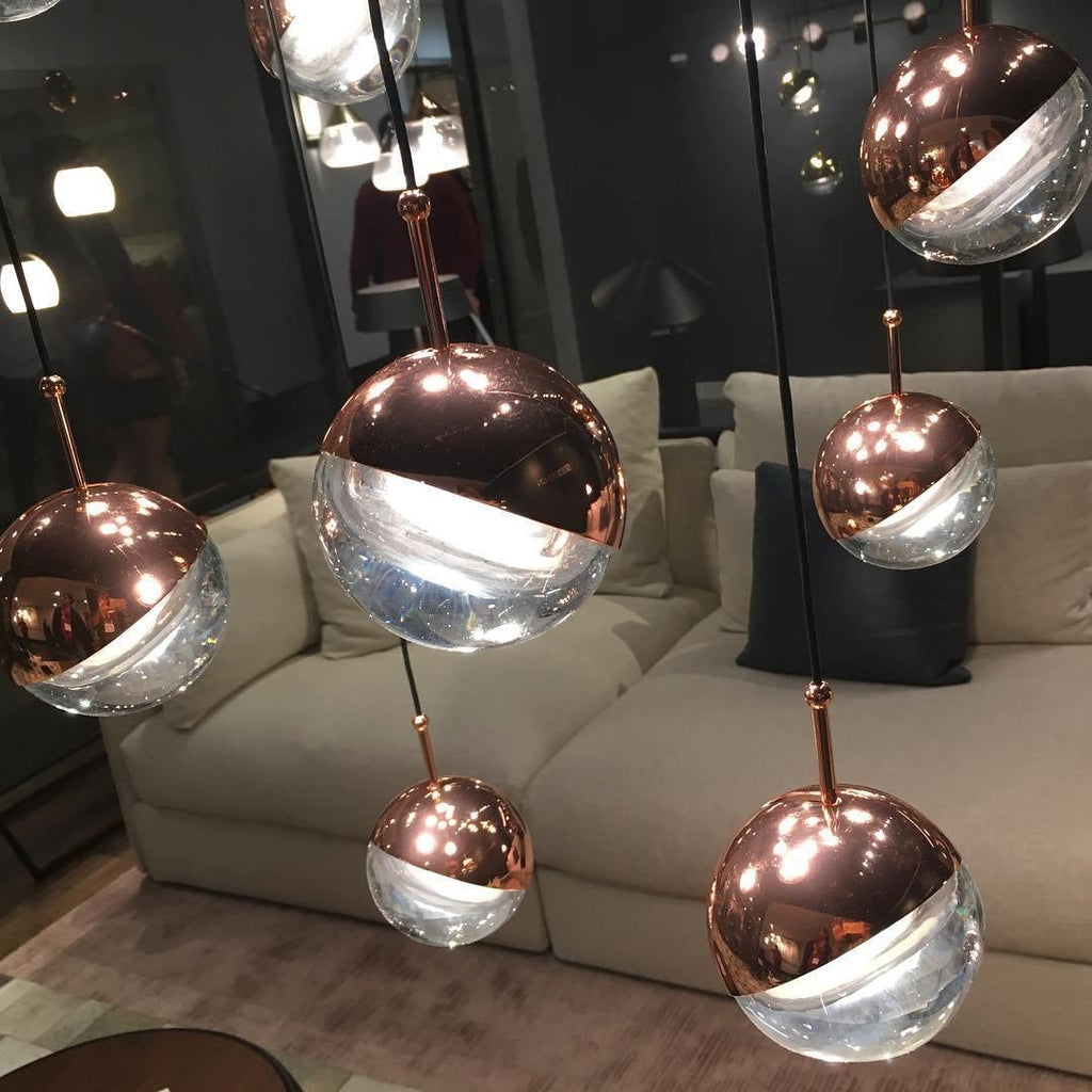 Close view of rose gold Clérachic globe pendants with clear glass lower halves, in front of a cream sofa.