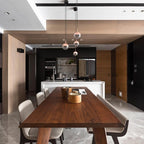 Rose gold Clérachic globe pendants hung at stepped heights above a long walnut dining table, with an island kitchen behind.