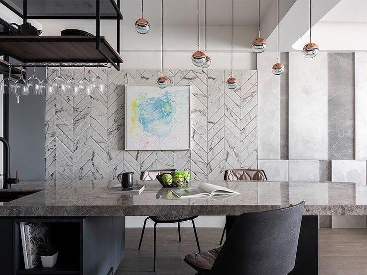 Row of small Clérachic globe pendants above a stone-topped table, with a glass rack and an abstract painting on a herringbone wall.