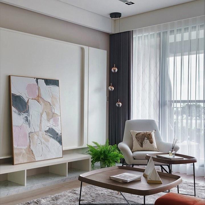 Rose gold Clérachic globe pendants on long drops by a tall window with sheer curtains, beside an armchair and a large painting.