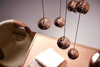 Looking down on four rose gold Clérachic globe pendants over a wooden desk with a notebook and a leather chair.