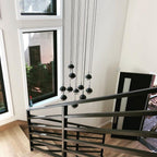 Clérachic pendants with matt black caps and clear lower halves hung in a tall stairwell beside a window and a black railing.
