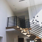 Strings of Clérachic pendants with dark caps and clear globes falling past a black railing, in a double-height stairwell.