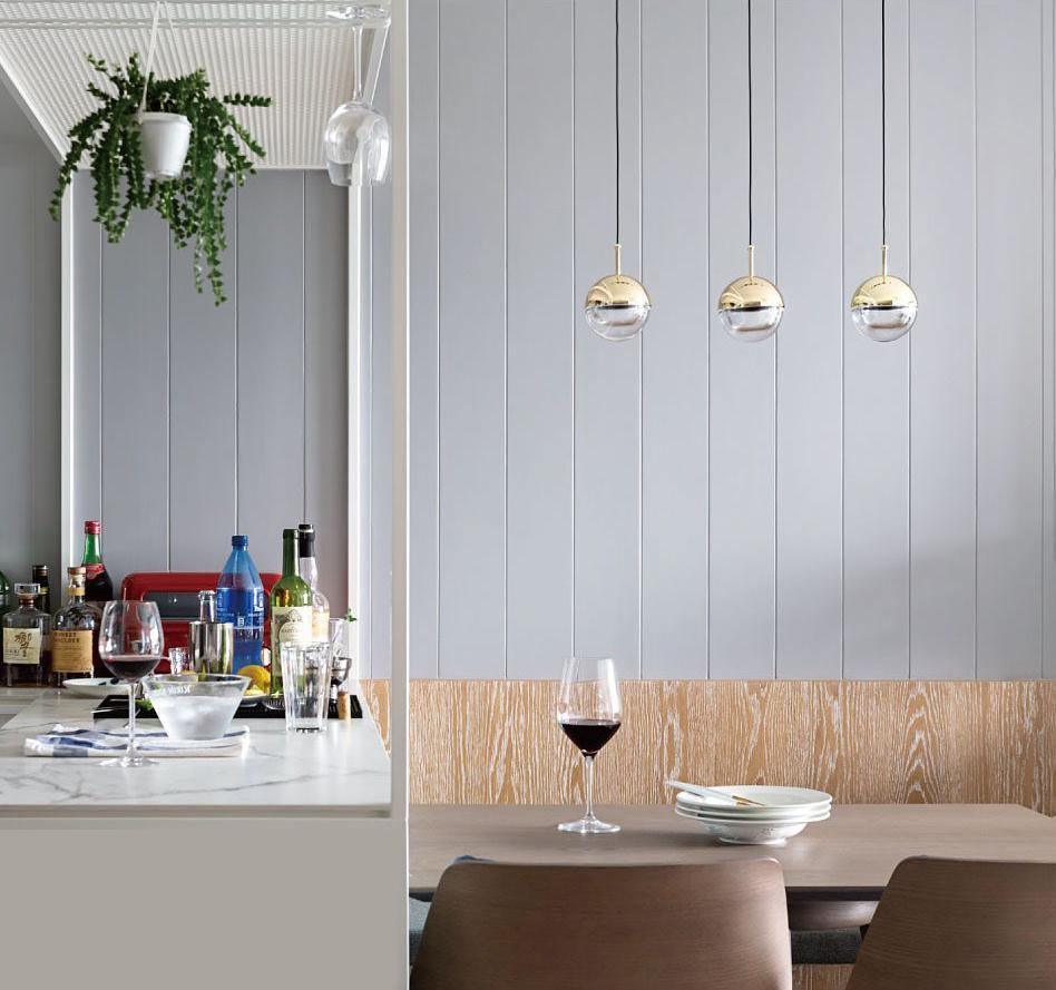 Three gold-finish Clérachic globe pendants against a pale panelled wall, above a dining table with a glass of red wine.