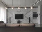 A row of five Clérachic globe pendants across a living room, in front of a marble wall with a wall-mounted television.