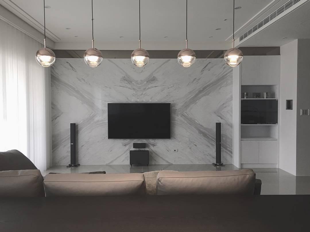 A row of five Clérachic globe pendants across a living room, in front of a marble wall with a wall-mounted television.