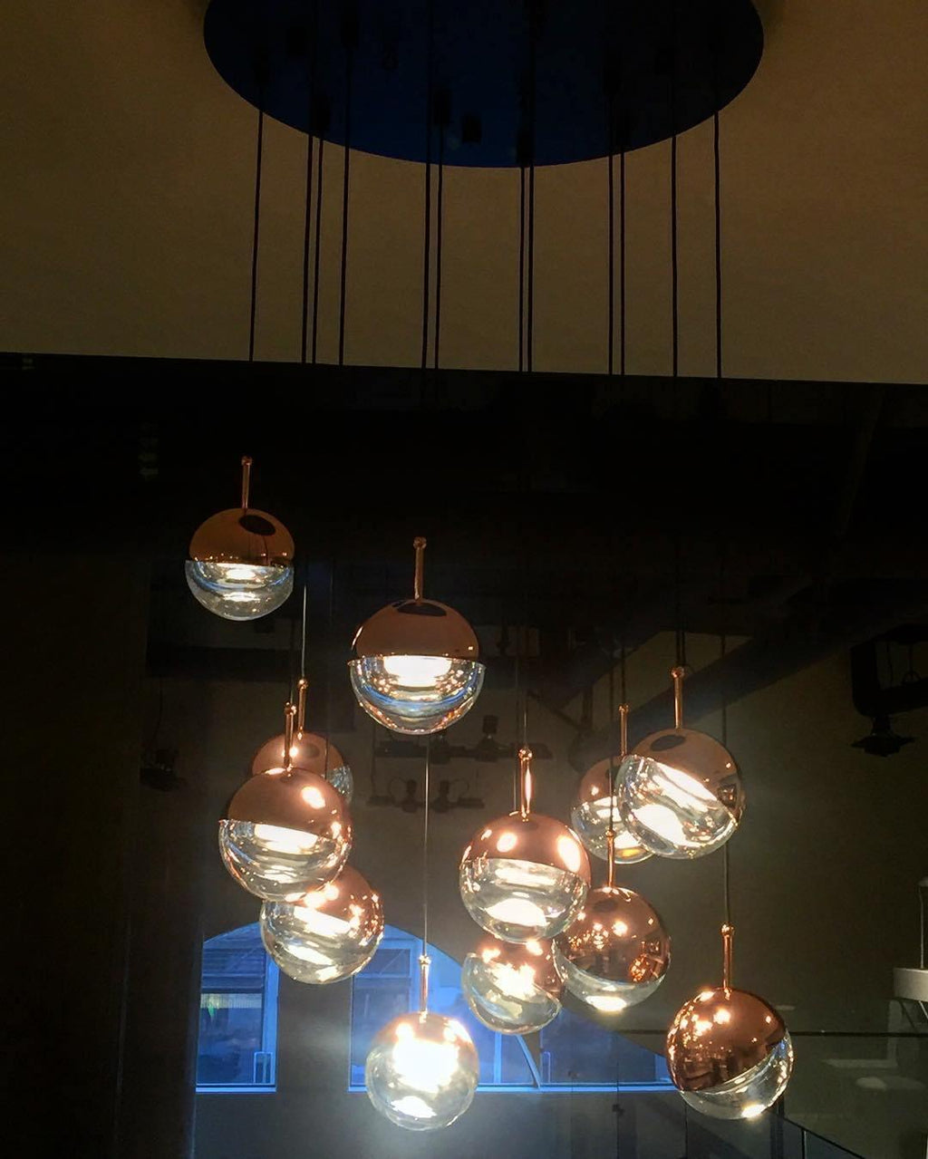 Rose gold and clear Clérachic globe pendants glowing in a cluster, photographed at night from a ceiling plate above.