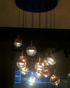 Rose gold and clear Clérachic globe pendants glowing in a cluster, photographed at night from a ceiling plate above.
