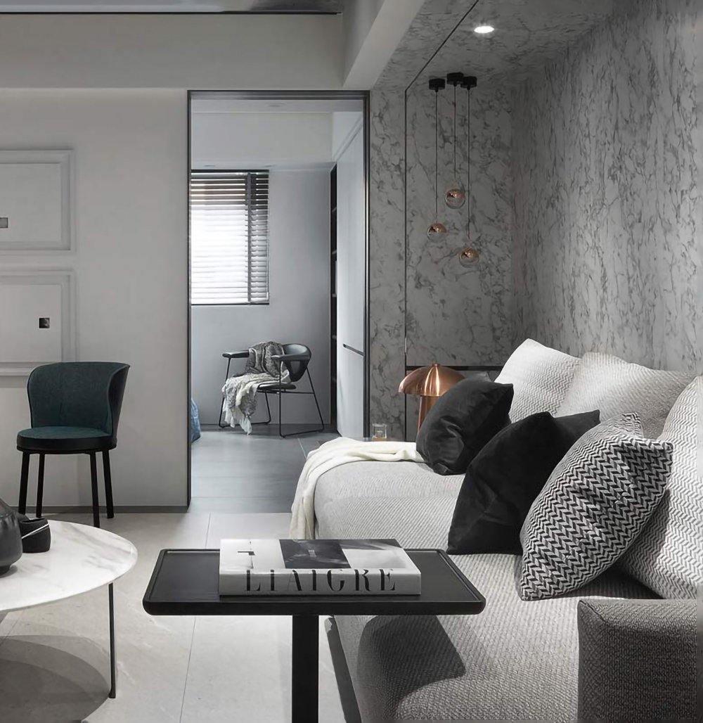 Clérachic globe pendants glowing softly beside a marble feature wall, with a grey sofa and a dark green armchair in the room.