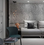 Small Clérachic pendants on staggered drops from a black canopy against a marbled wall, above a grey sofa and a teal chair.