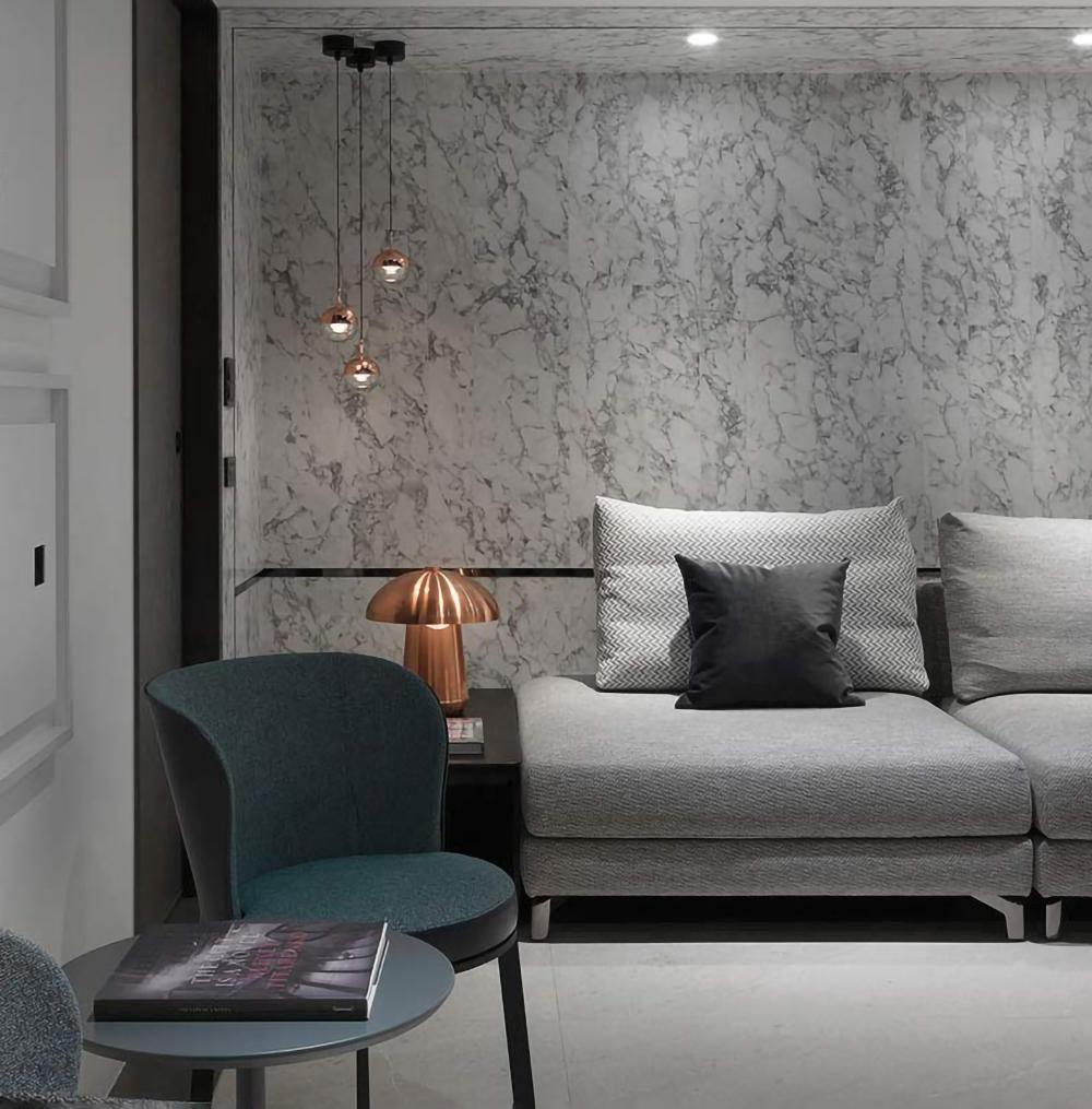 Small Clérachic pendants on staggered drops from a black canopy against a marbled wall, above a grey sofa and a teal chair.