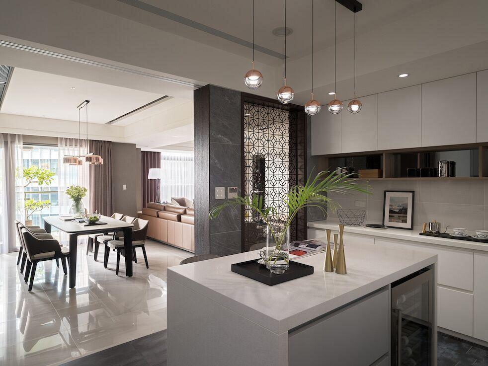 Rose gold Clérachic globe pendants in a row over a white kitchen island, with a dining table and a living area beyond.
