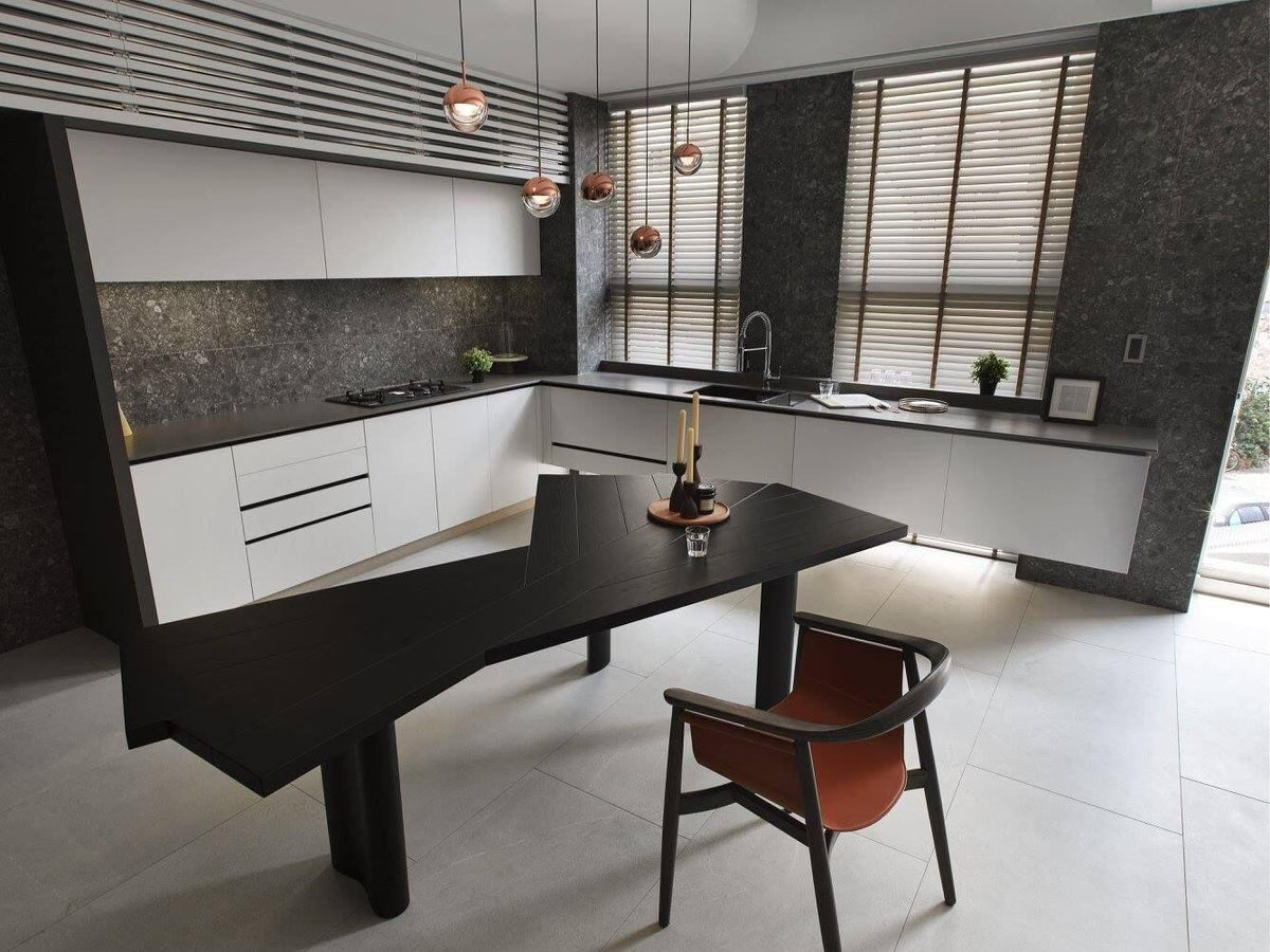 Rose gold Clérachic globe pendants hung over a dark, angular dining table in an open white kitchen with louvred blinds.