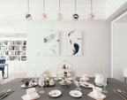 Five Clérachic globe pendants with rose gold caps in a row above a laid afternoon-tea table, with feather prints on the wall.