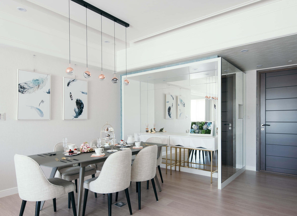 A row of Clérachic globe pendants on a black rail above a grey dining table with cream chairs and a mirrored wall.