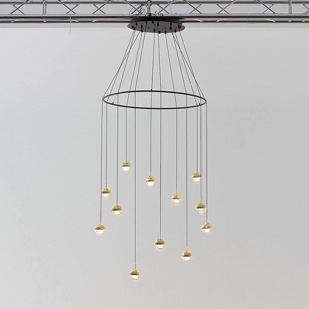 Clérachic ring chandelier with clear glass globes and gold-toned caps hung from a black ceiling plate under a ceiling truss.