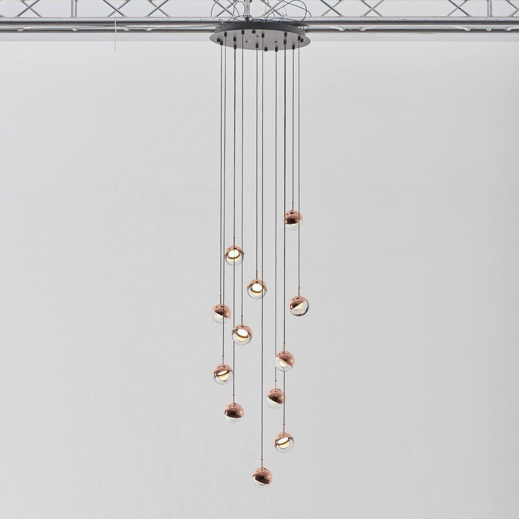 Cluster of Clérachic globe pendants with rose gold caps on cords of varied length from a black ceiling plate.