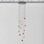 Cluster of Clérachic globe pendants with rose gold caps on cords of varied length from a black ceiling plate.