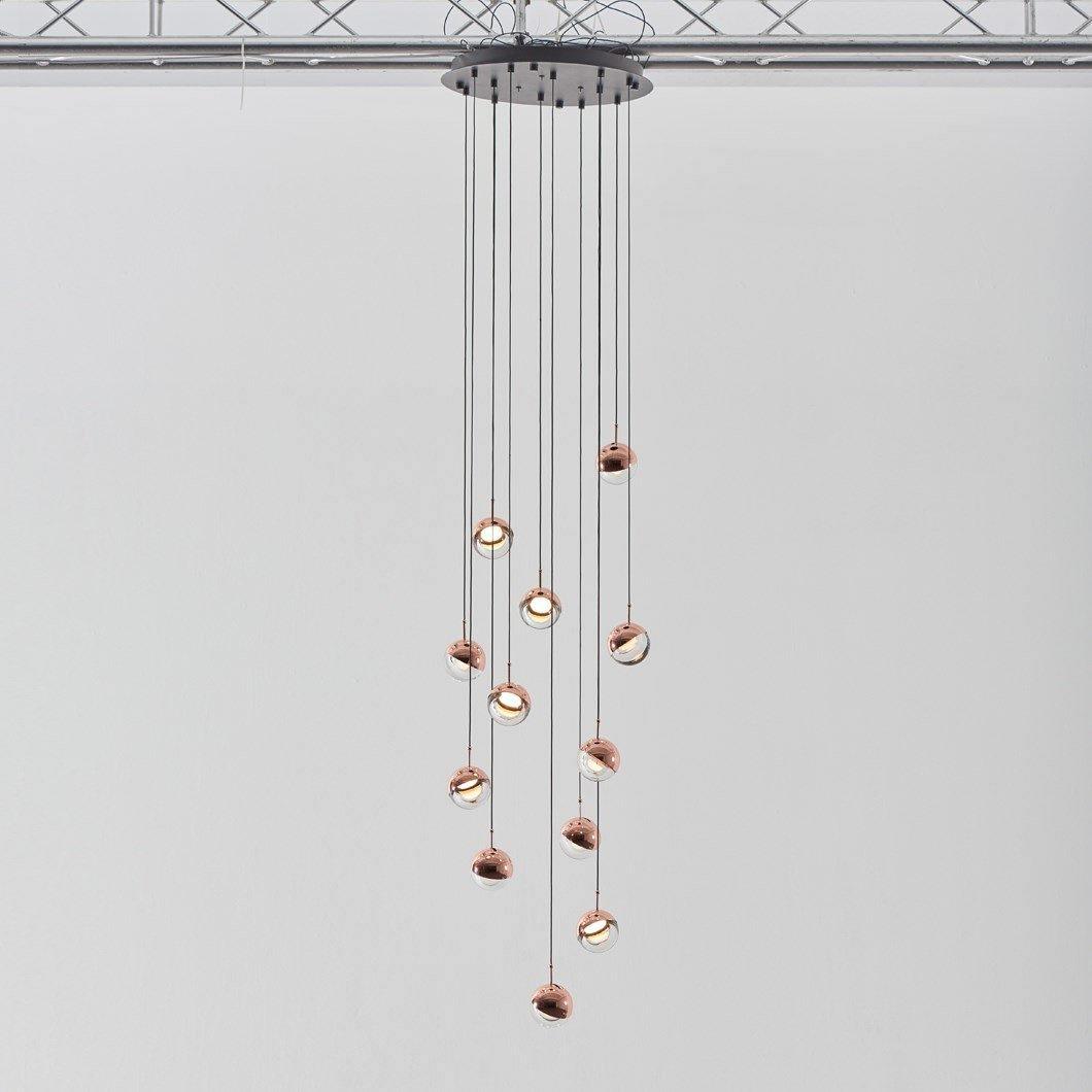 Cluster of Clérachic globe pendants with rose gold caps on cords of varied length from a black ceiling plate.