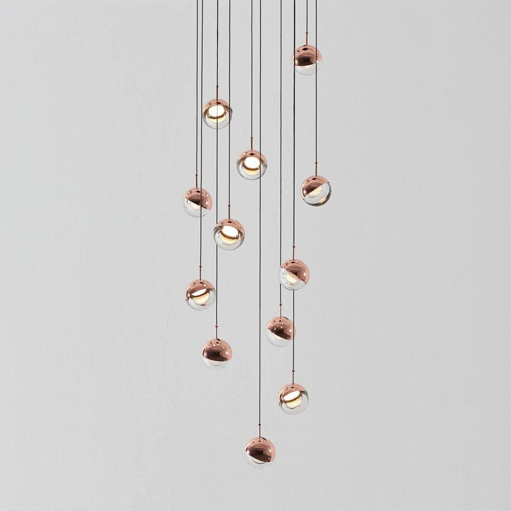 Cluster of Clérachic globe pendants with rose gold caps and clear lower halves hanging at varied heights on a pale grey backdrop.