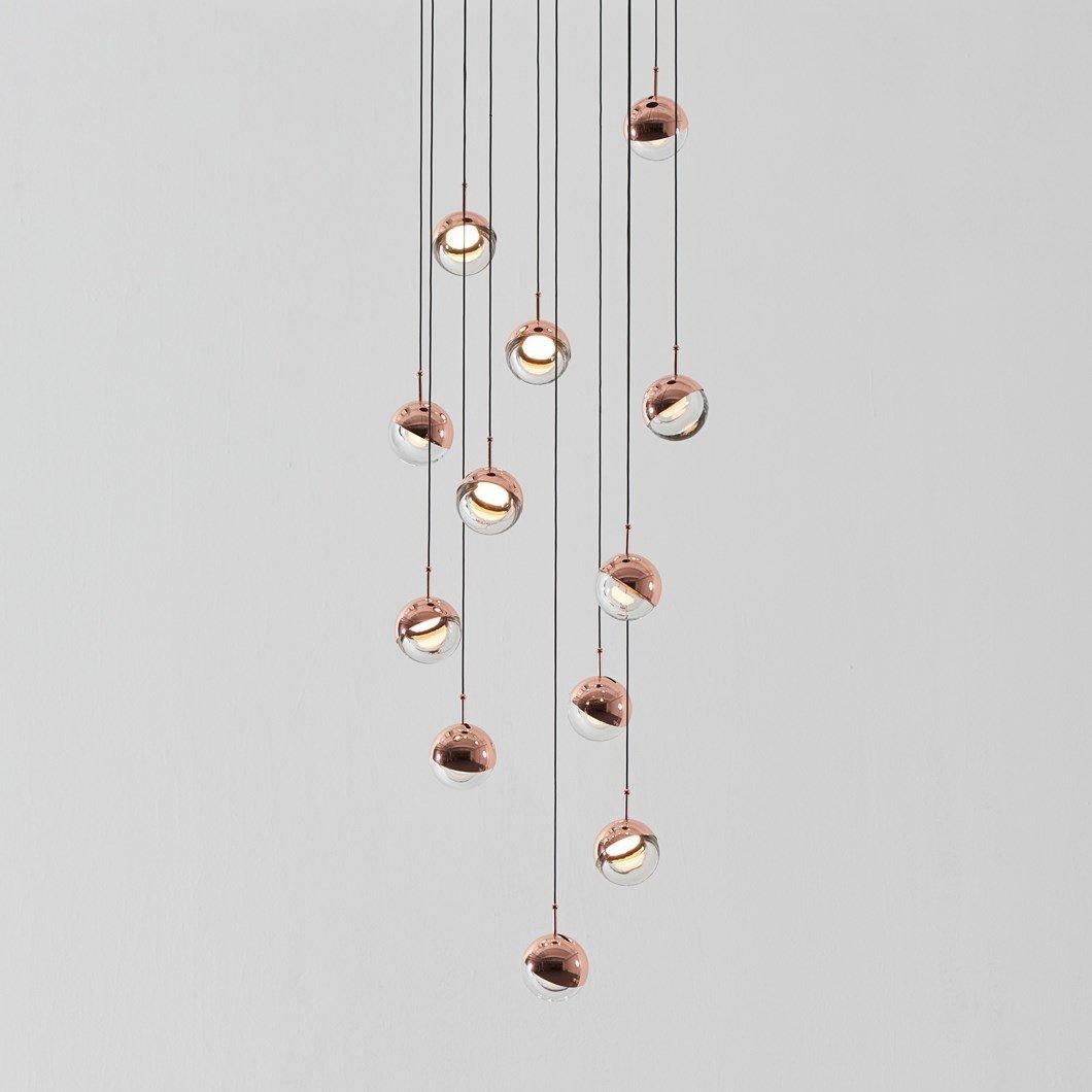 Cluster of Clérachic globe pendants with rose gold caps and clear lower halves hanging at varied heights on a pale grey backdrop.