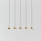 Five gold-finish Clérachic globe pendants hung in a straight line on thin cords against a pale grey backdrop.