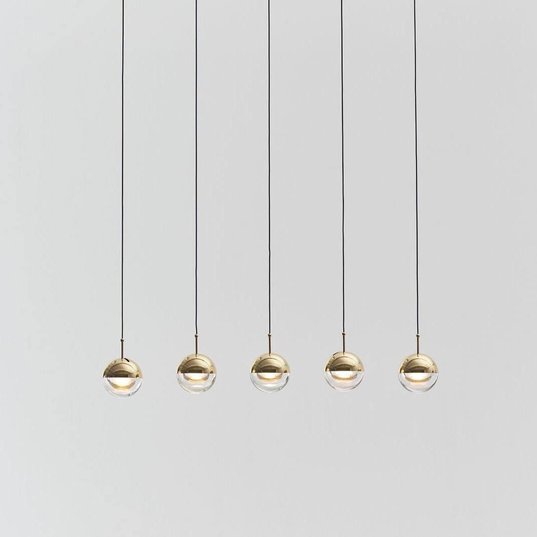 Five gold-finish Clérachic globe pendants hung in a straight line on thin cords against a pale grey backdrop.