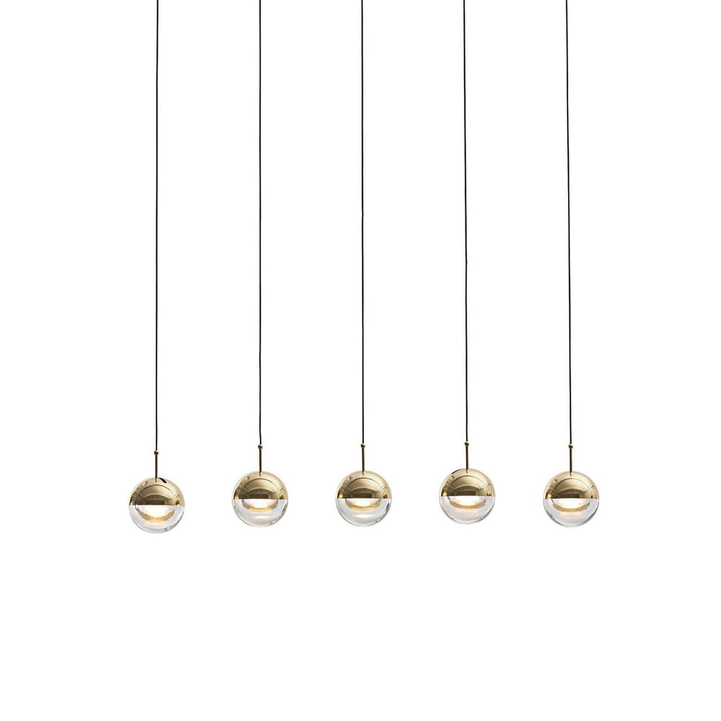 Five gold-finish Clérachic globe pendants in a row, each with a clear glass lower half and a lit LED, on a pale grey backdrop.