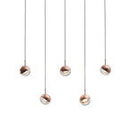 Five rose gold Clérachic globe pendants hung at staggered heights on a pale backdrop, each with a clear glass lower half.