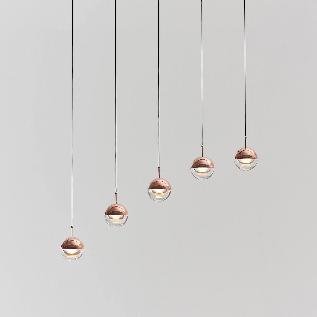 Five rose gold Clérachic globe pendants hung in a rising diagonal line, on a pale grey backdrop.