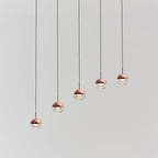 Five rose gold Clérachic globe pendants hung in a rising diagonal line, on a pale grey backdrop.