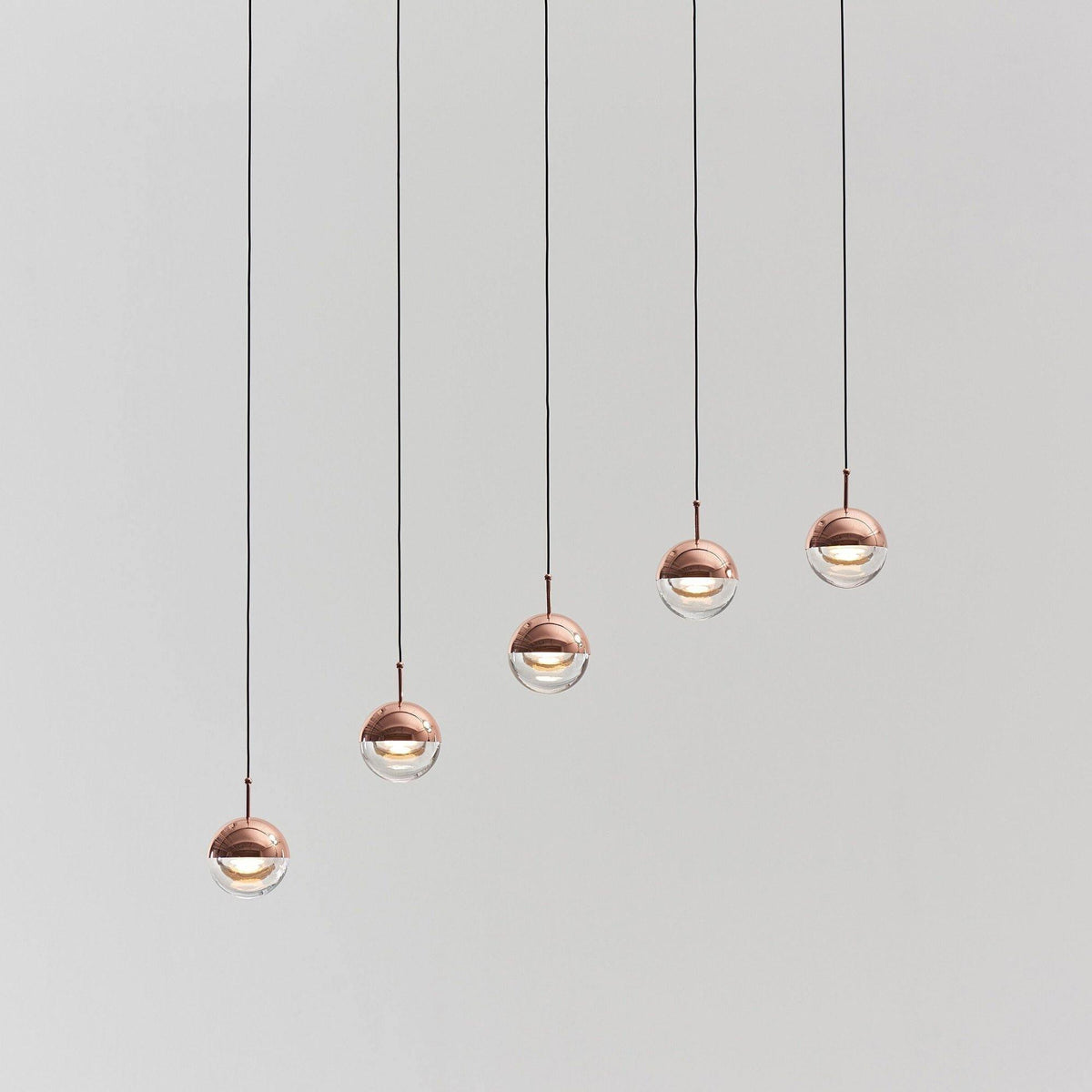 Five rose gold Clérachic globe pendants hung in a rising diagonal line, on a pale grey backdrop.