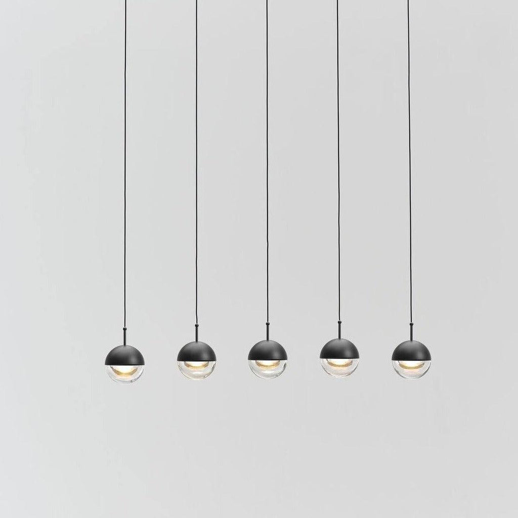 Five Clérachic globe pendants with matt black caps and clear lower halves, hung in a row on thin cords against a pale grey backdrop.