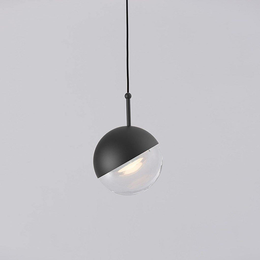 Close view of a matt black Clérachic globe pendant, its black half-cap over a clear glass half with a warm LED inside.